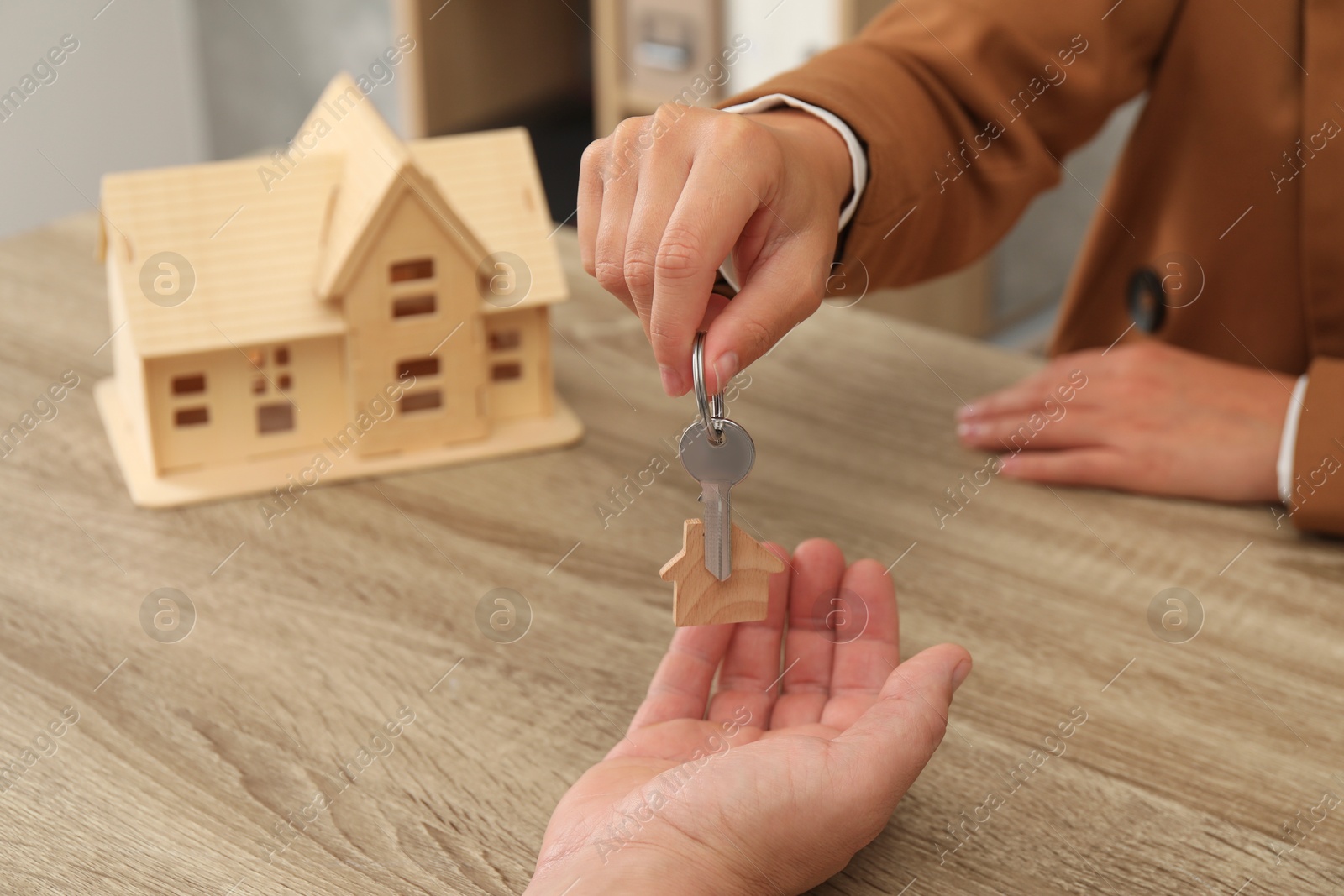 Photo of Real estate agent giving house key to new owner at wooden table, closeup