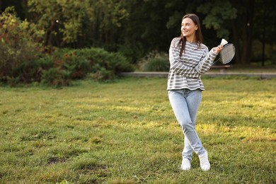 Happy young woman with badminton racket and shuttlecock in park, space for text