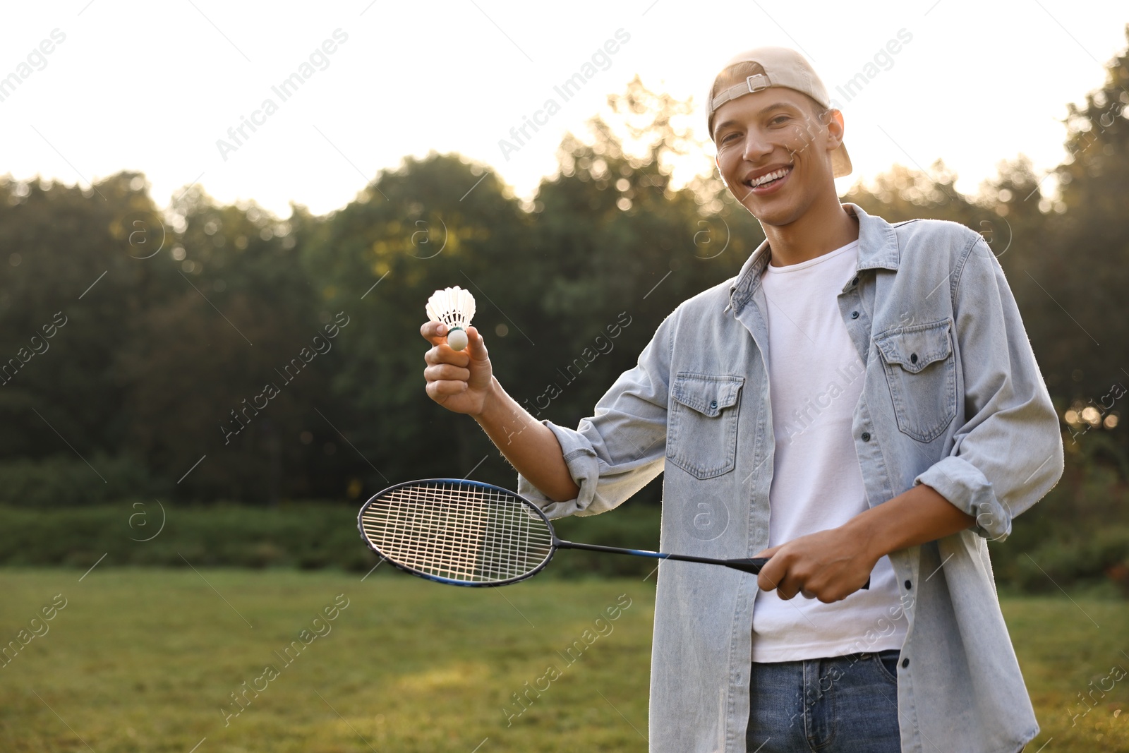 Photo of Happy young man with badminton racket and shuttlecock in park, low angle view