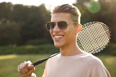 Happy young man with badminton racket in park on sunny day