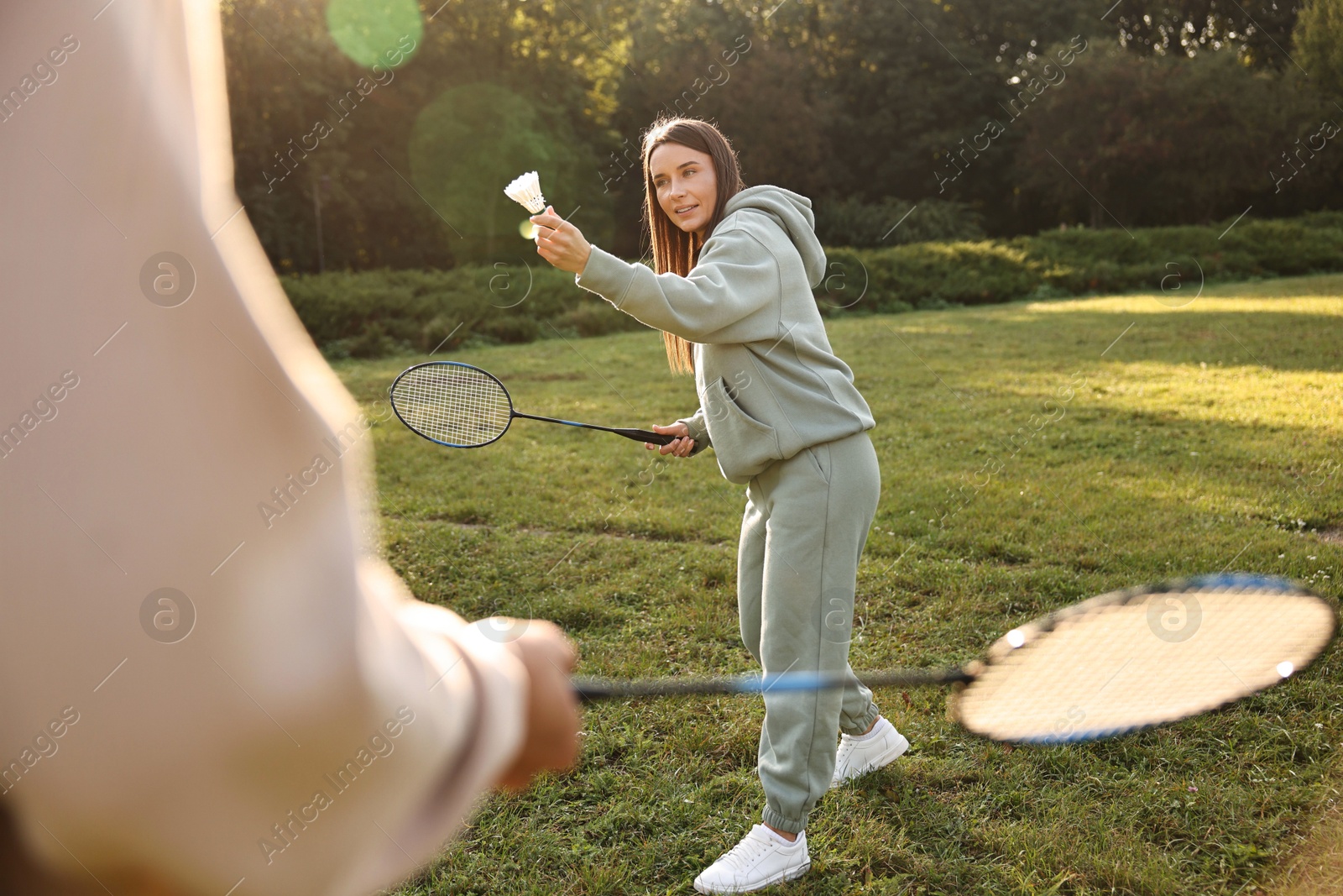 Photo of Young woman and man playing badminton in park on sunny day, selective focus