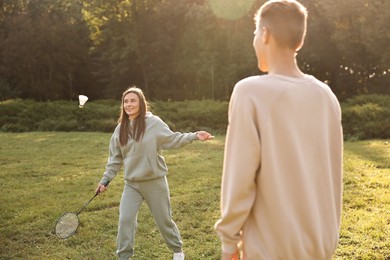 Photo of Young woman and man playing badminton in park on sunny day, selective focus