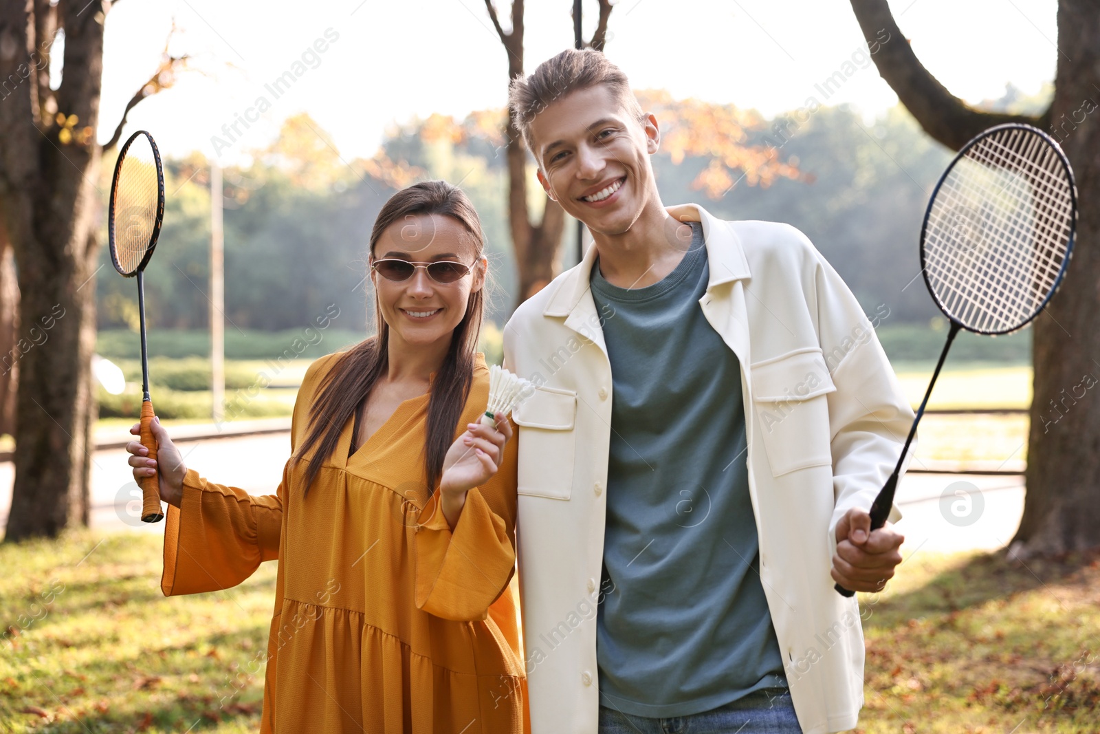 Photo of Young man and woman with badminton rackets and shuttlecock in park on sunny day