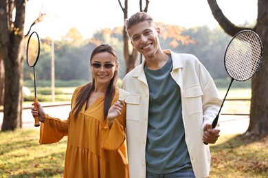 Young man and woman with badminton rackets and shuttlecock in park on sunny day