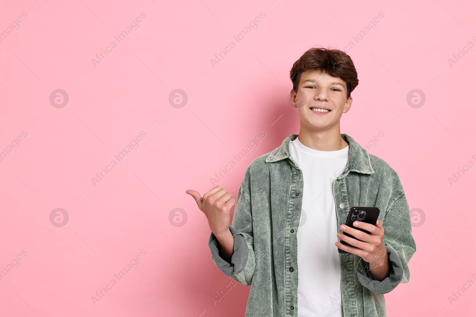 Photo of Happy teenage boy with smartphone on pink background, space for text