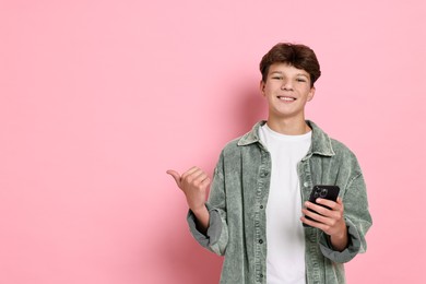 Photo of Happy teenage boy with smartphone on pink background, space for text