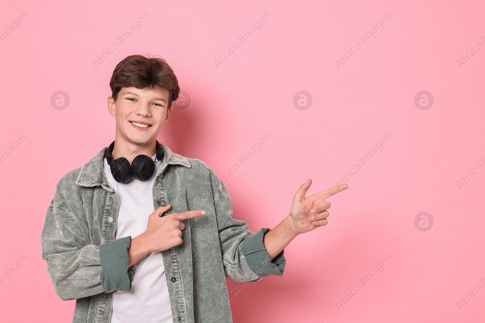 Photo of Happy teenage boy with headphones on pink background, space for text