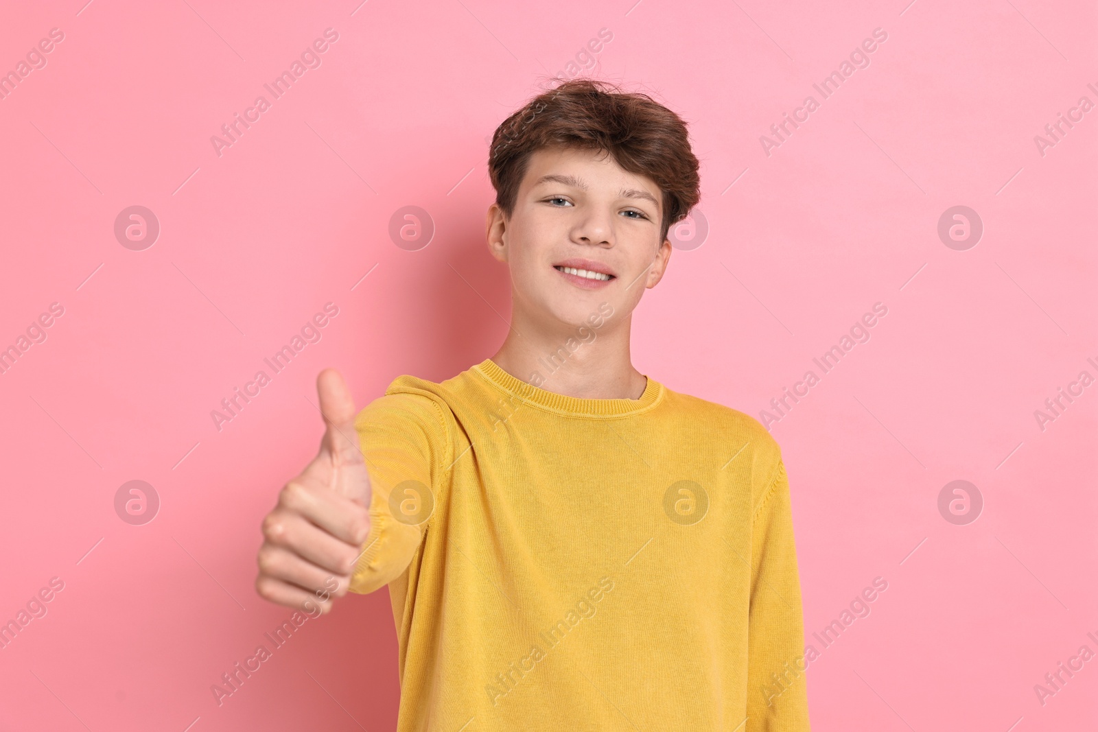 Photo of Happy teenage boy showing thumbs up on pink background