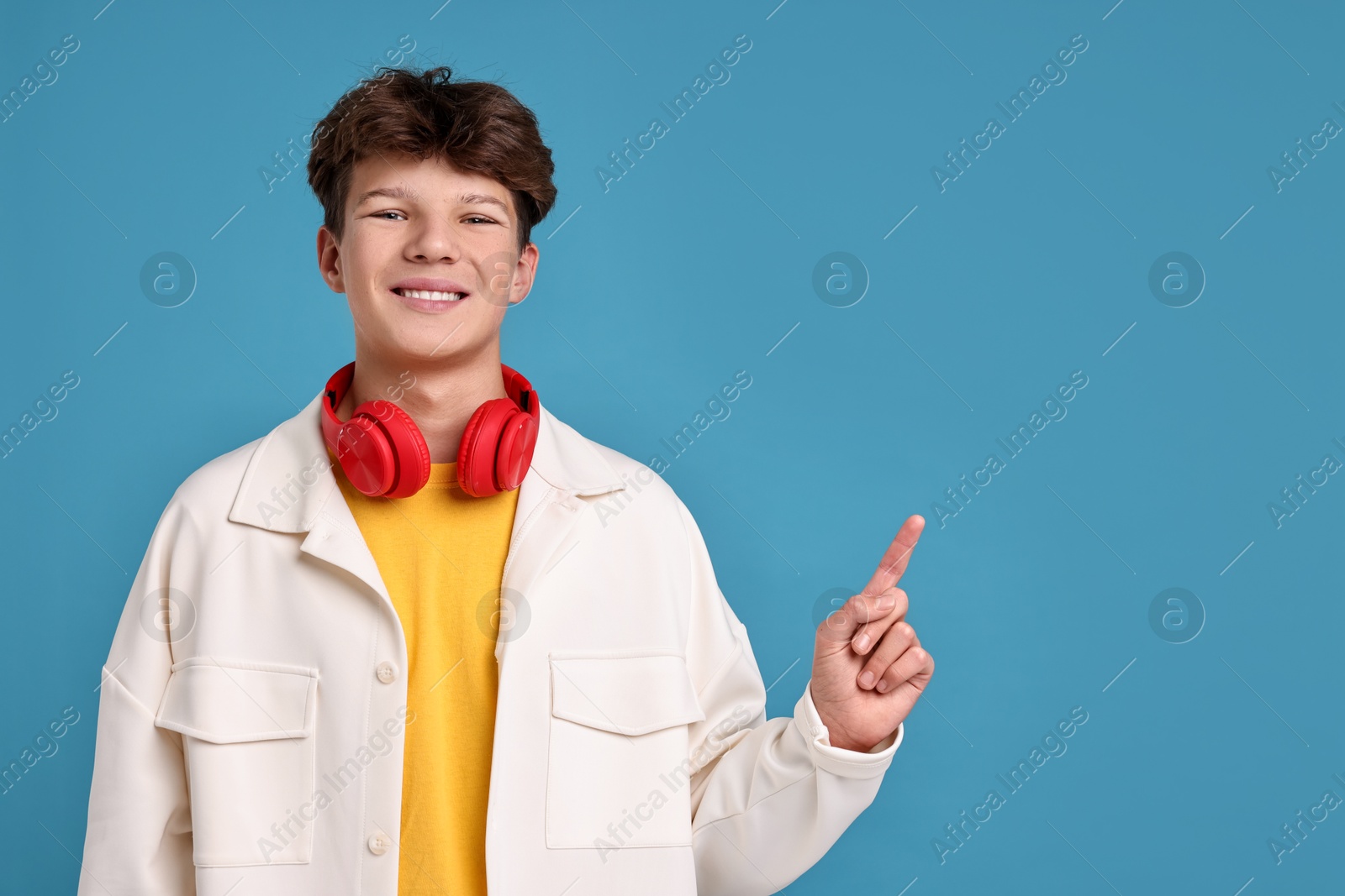 Photo of Happy teenage boy with headphones on light blue background, space for text