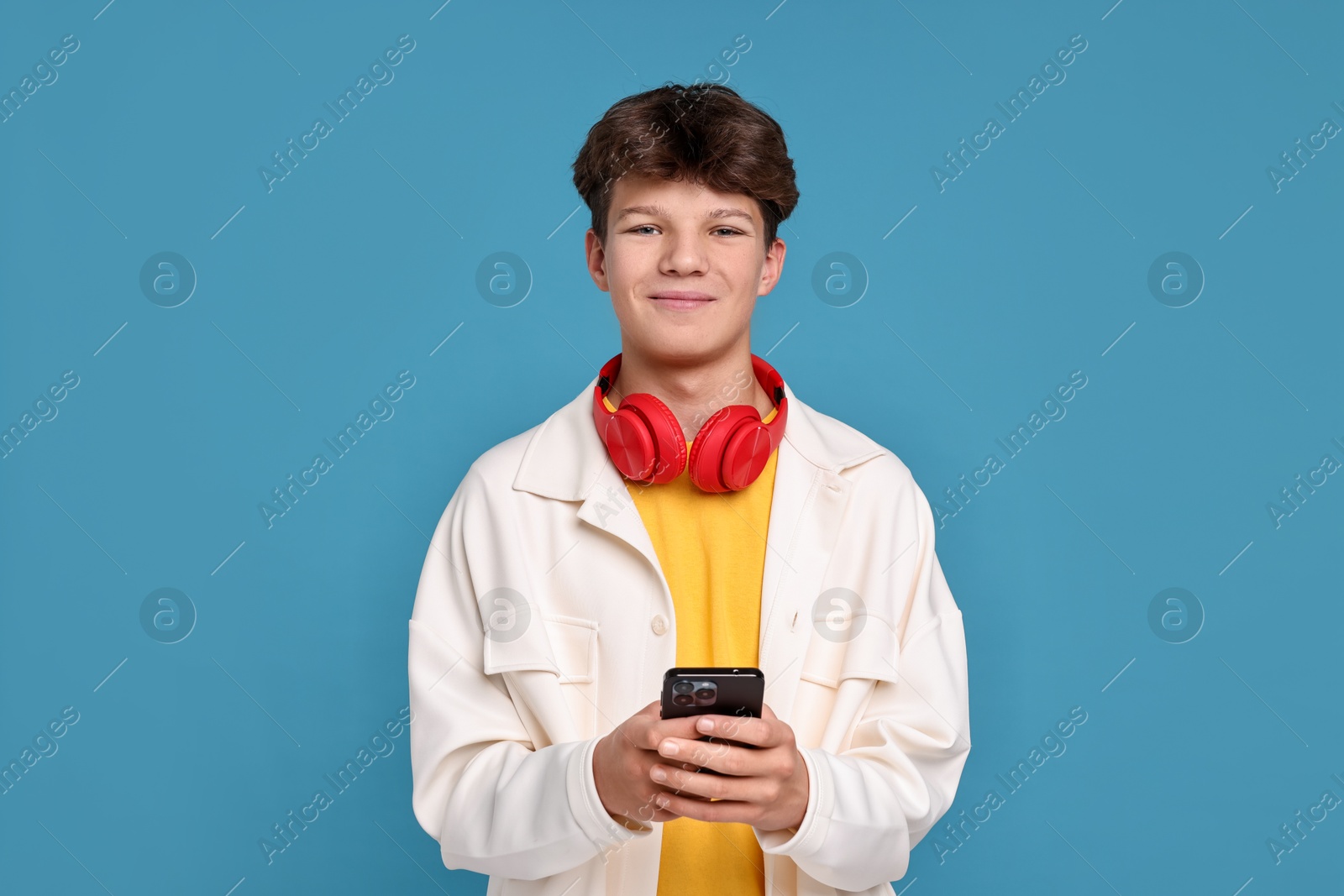 Photo of Teenage boy with headphones and smartphone on light blue background