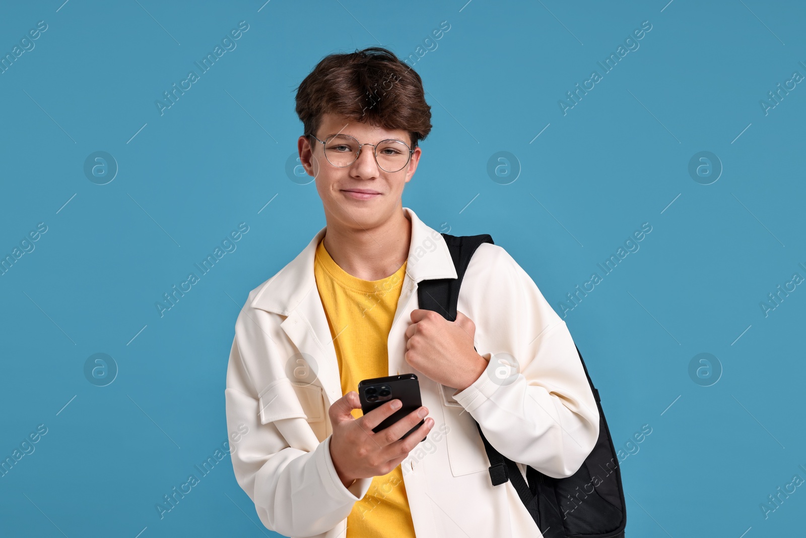 Photo of Teenage boy with smartphone and backpack on light blue background