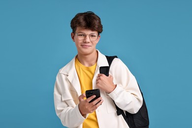 Photo of Teenage boy with smartphone and backpack on light blue background