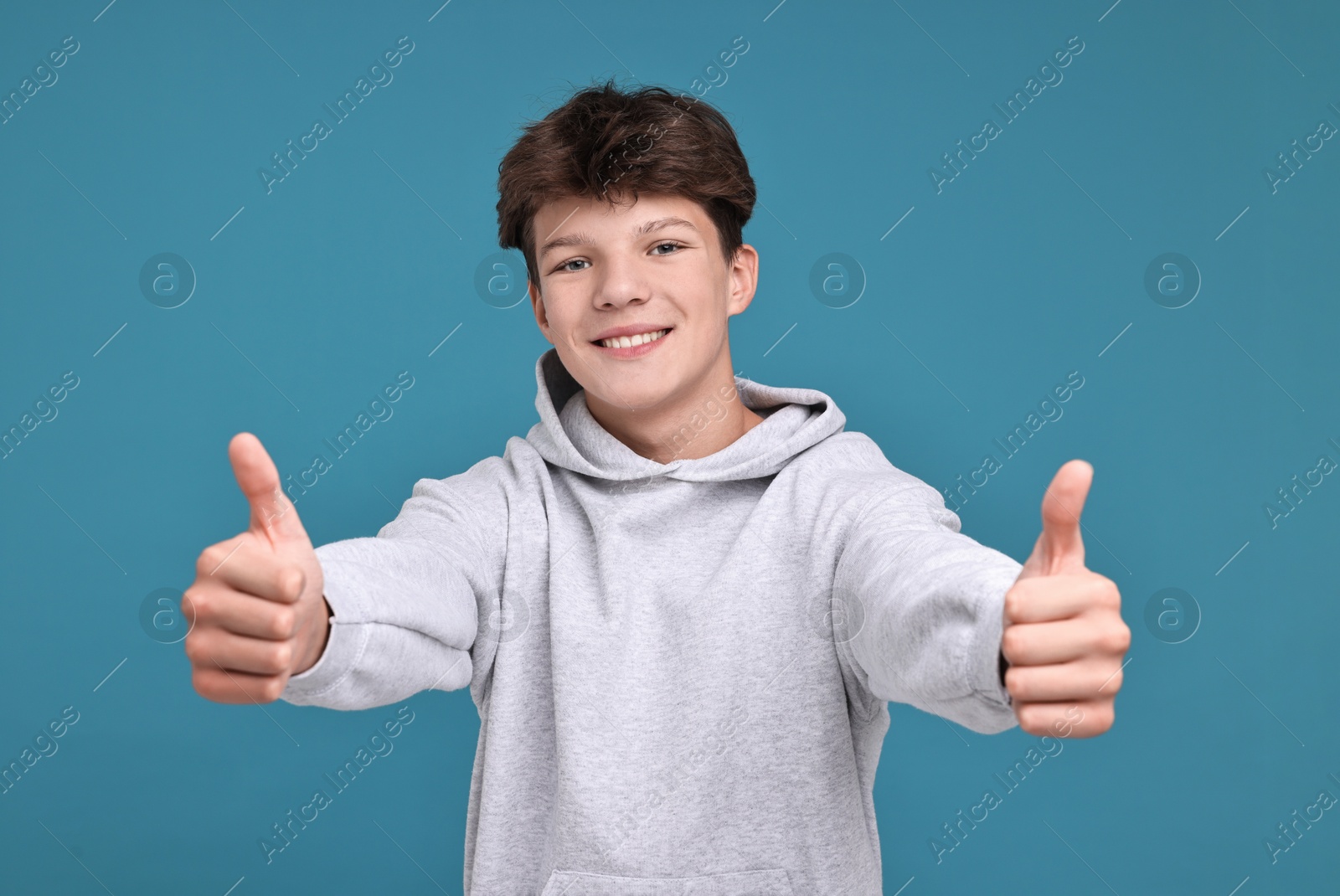 Photo of Happy teenage boy showing thumbs up on light blue background