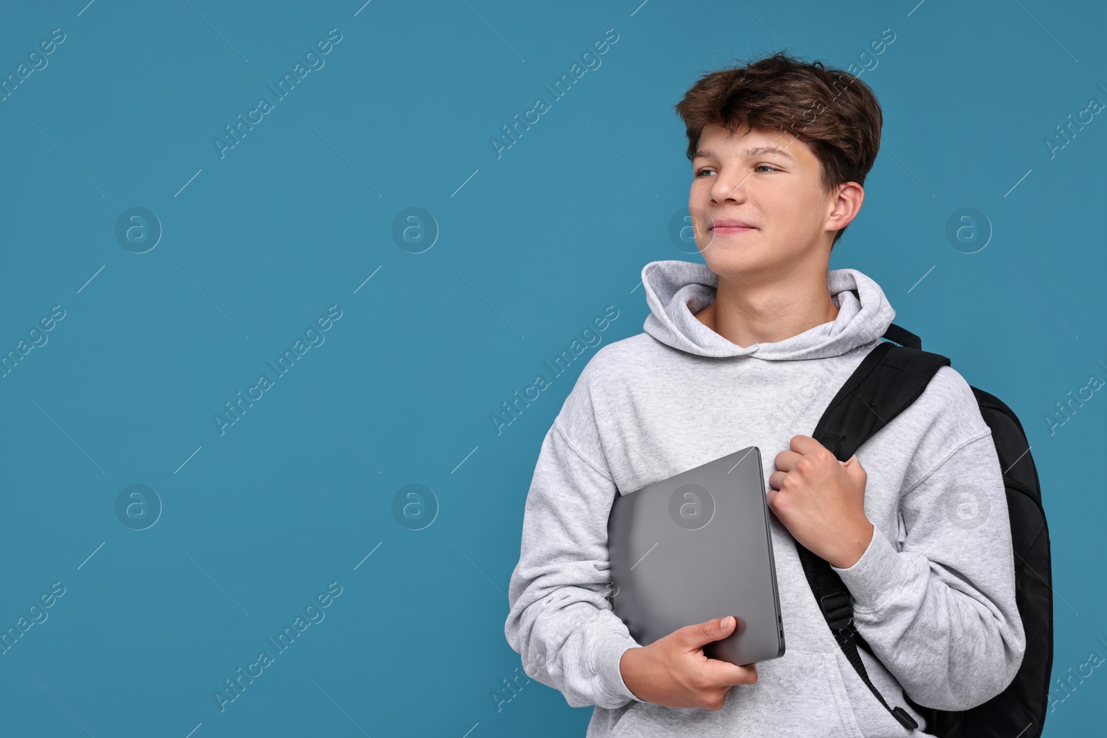 Photo of Teenage boy with laptop and backpack on light blue background, space for text