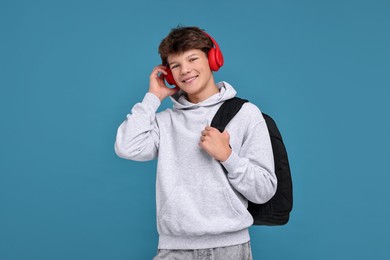 Photo of Teenage boy in headphones with backpack on light blue background