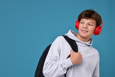 Photo of Teenage boy in headphones with backpack on light blue background, space for text