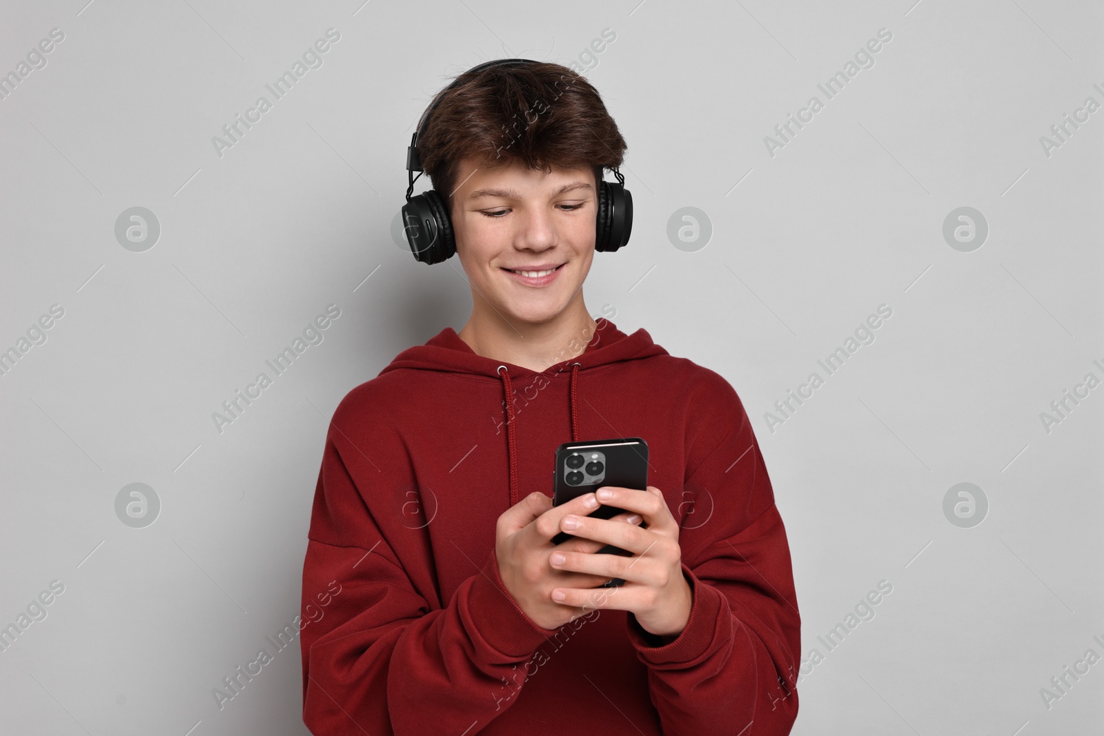 Photo of Teenage boy in headphones with smartphone on light grey background