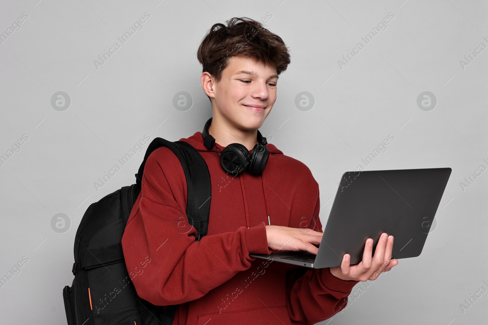 Photo of Teenage boy with headphones, laptop and backpack on light grey background