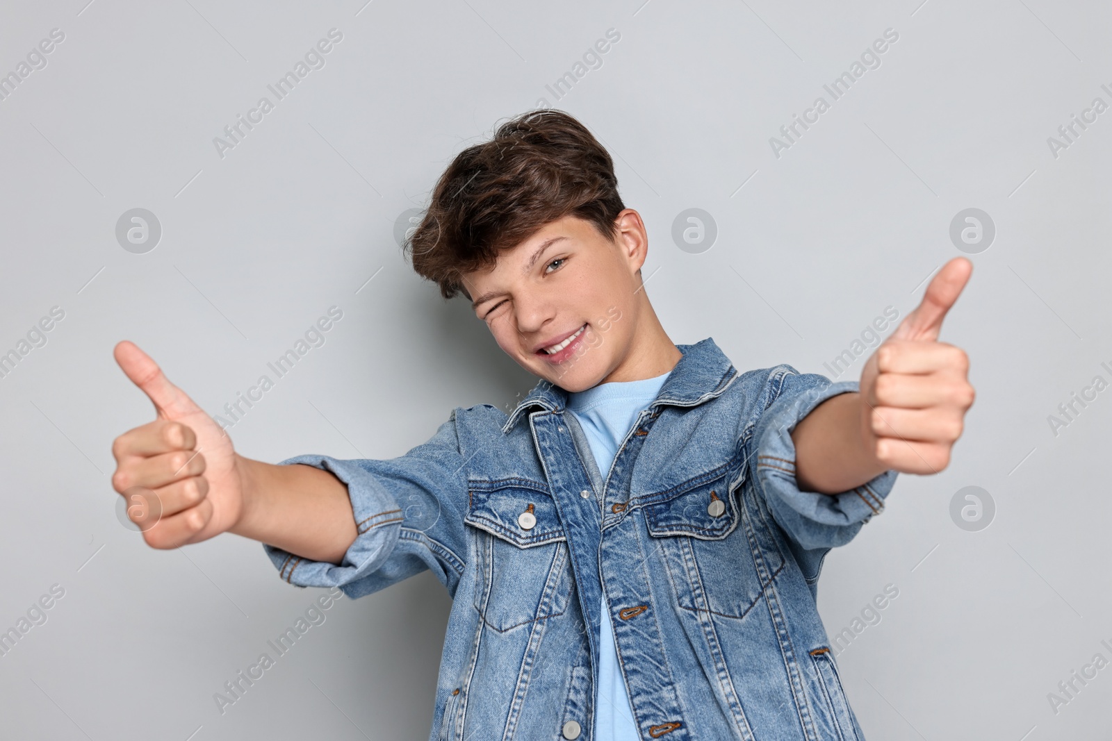 Photo of Happy teenage boy showing thumbs up on light grey background