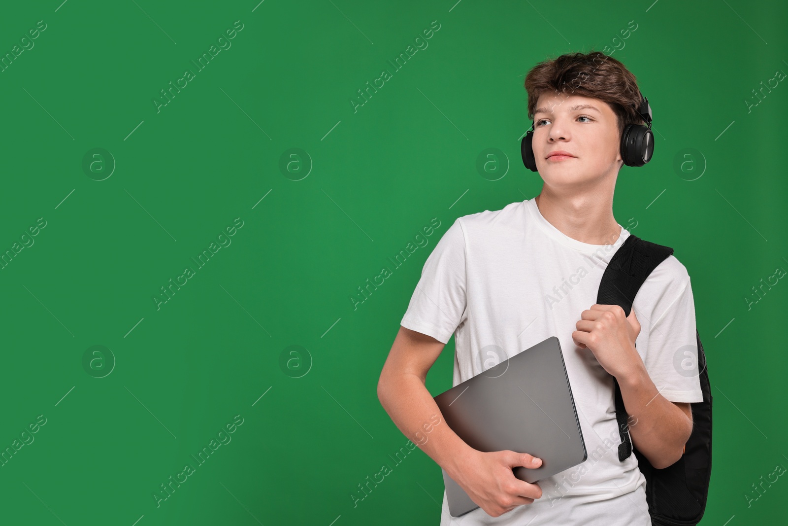 Photo of Teenage boy in headphones with laptop on green background, space for text