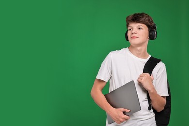 Photo of Teenage boy in headphones with laptop on green background, space for text