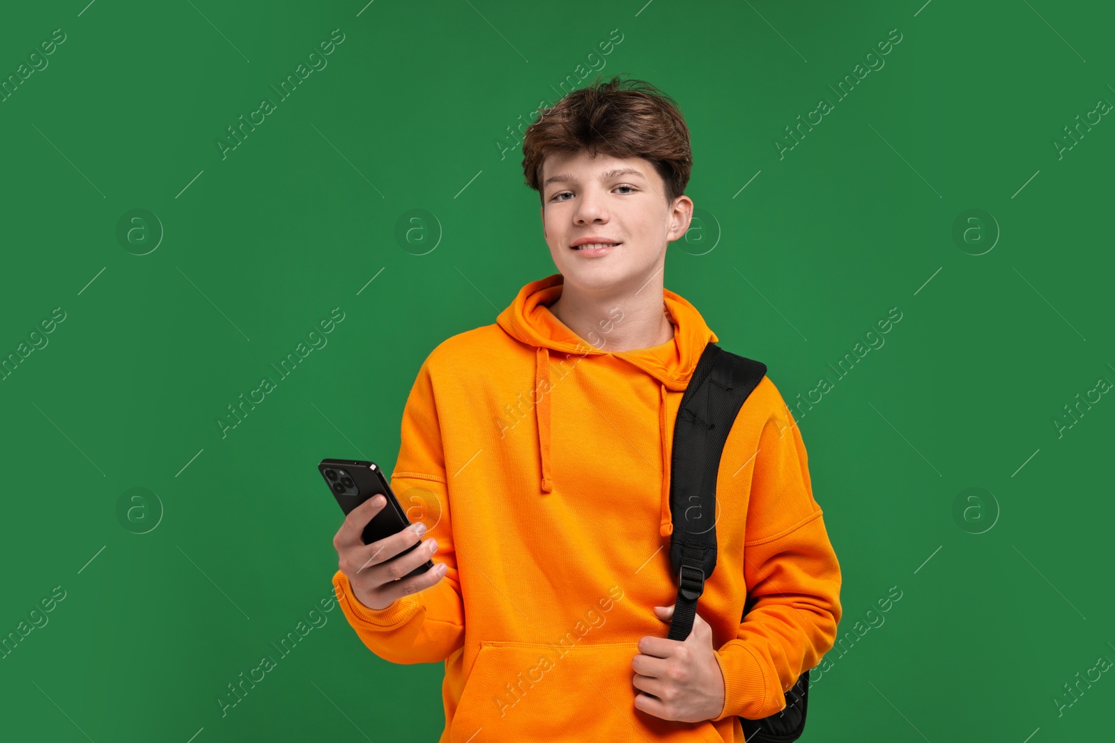 Photo of Teenage boy with smartphone and backpack on green background