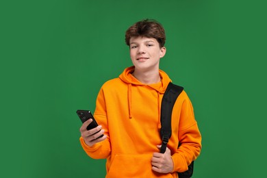 Photo of Teenage boy with smartphone and backpack on green background