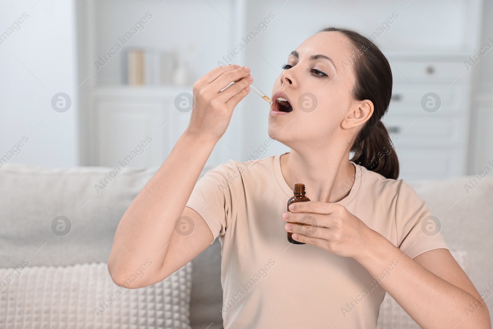 Photo of Young woman taking CBD tincture indoors. Herbal extract