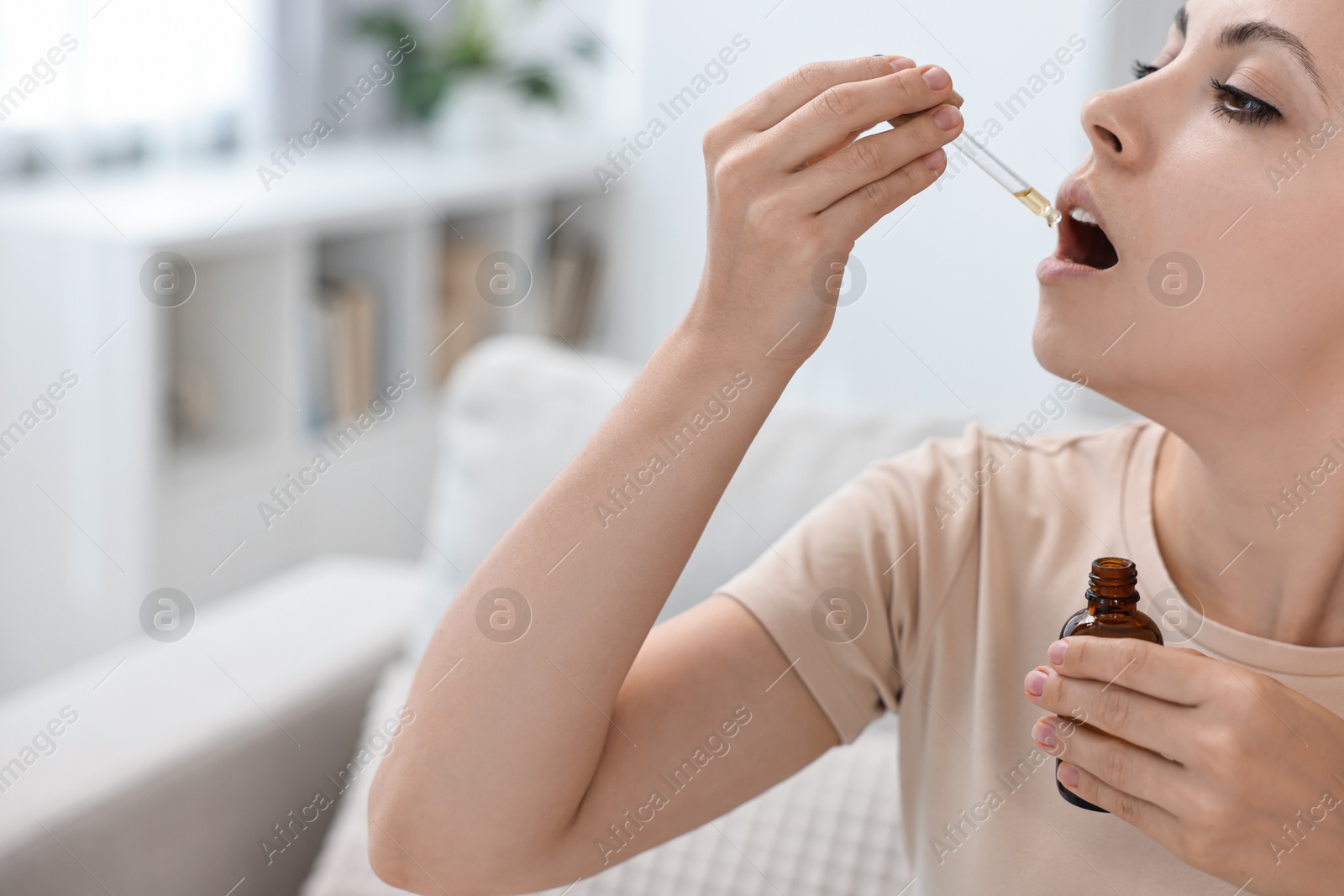 Photo of Young woman taking CBD tincture indoors. Herbal extract