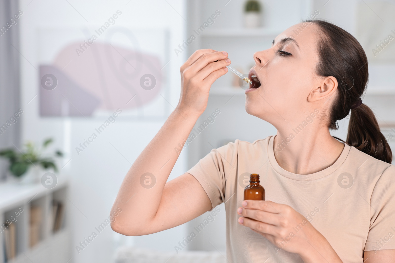 Photo of Young woman taking CBD tincture indoors. Herbal extract