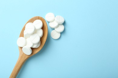 Photo of Antibiotic pills and spoon on light blue background, flat lay. Space for text