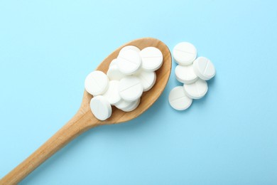 Photo of Antibiotic pills and spoon on light blue background, flat lay