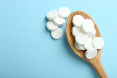 Photo of Antibiotic pills and spoon on light blue background, flat lay. Space for text