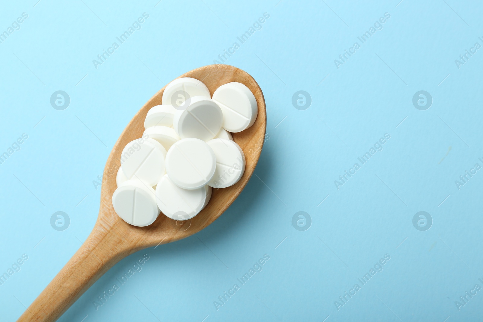 Photo of Antibiotic pills in spoon on light blue background, top view. Space for text