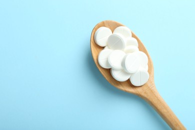 Photo of Antibiotic pills in spoon on light blue background, top view. Space for text