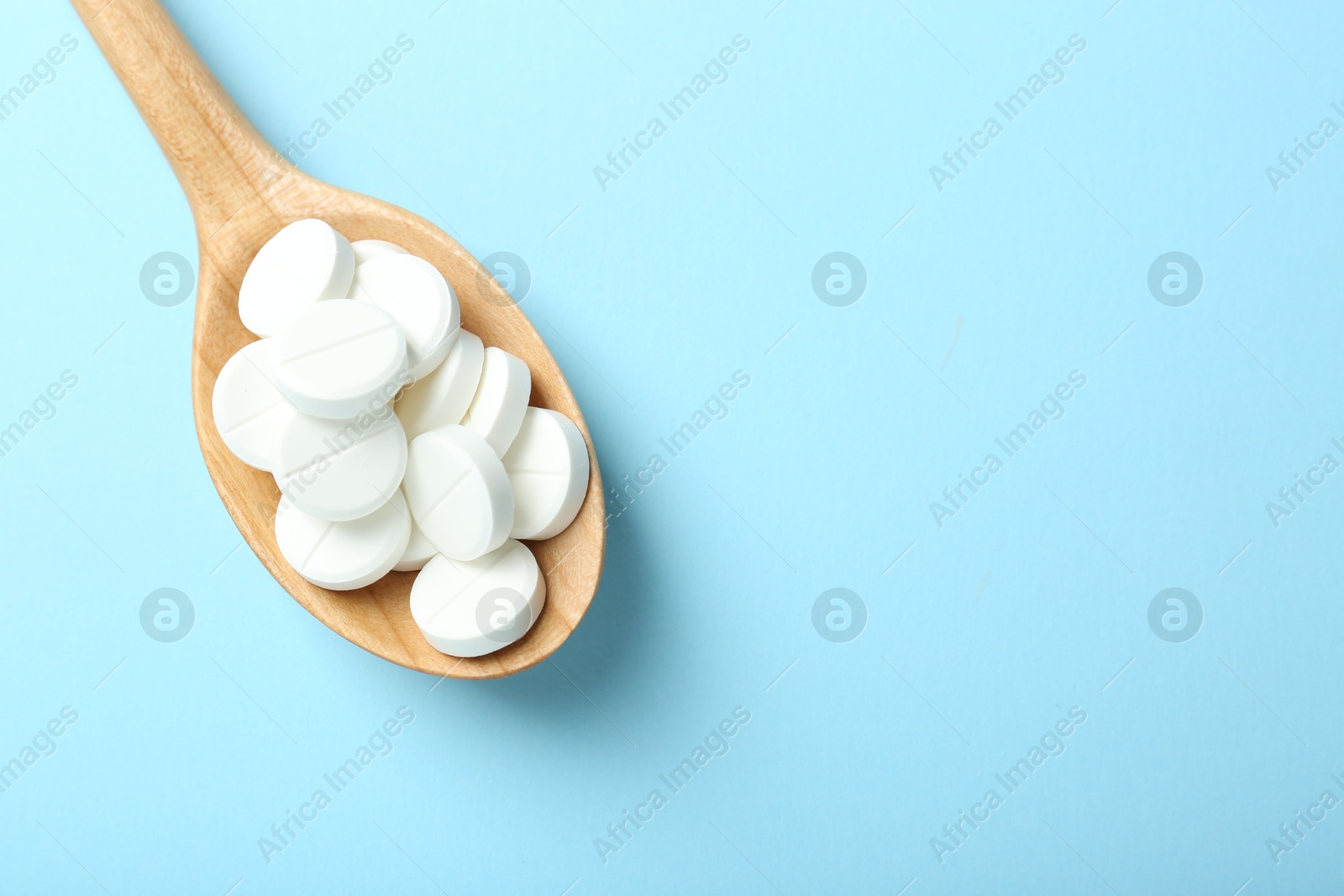 Photo of Antibiotic pills in spoon on light blue background, top view. Space for text