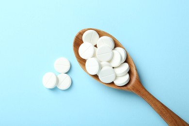 Photo of Antibiotic pills and spoon on light blue background, flat lay. Space for text