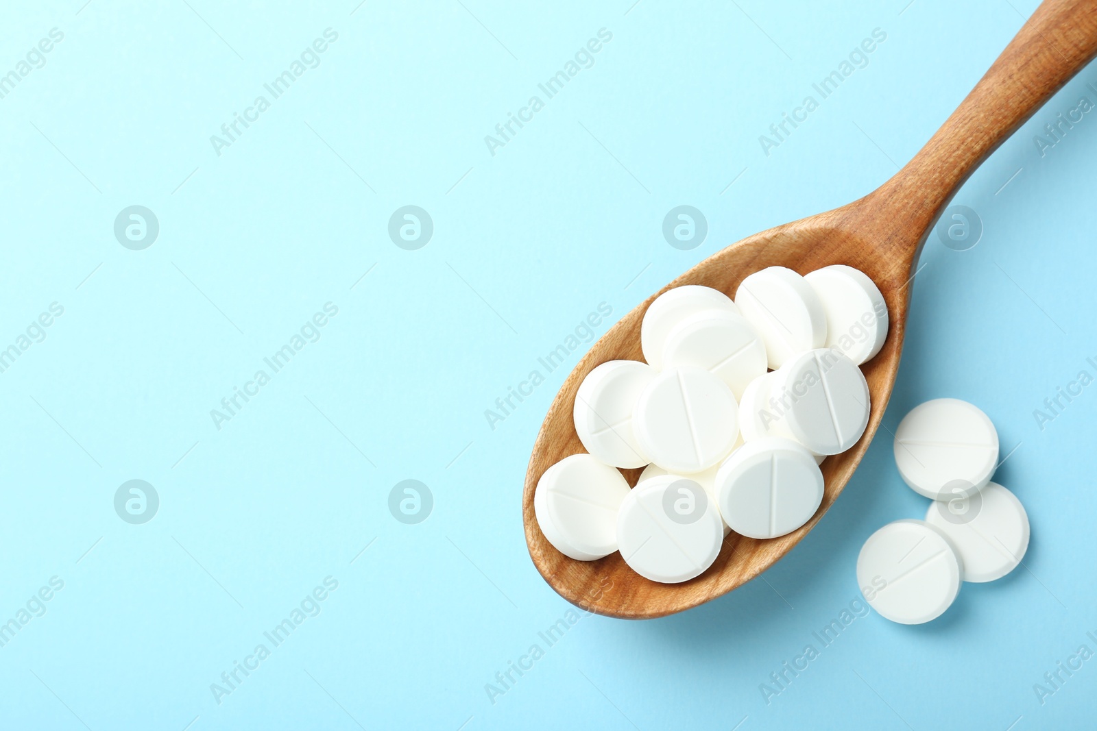 Photo of Antibiotic pills and spoon on light blue background, flat lay. Space for text