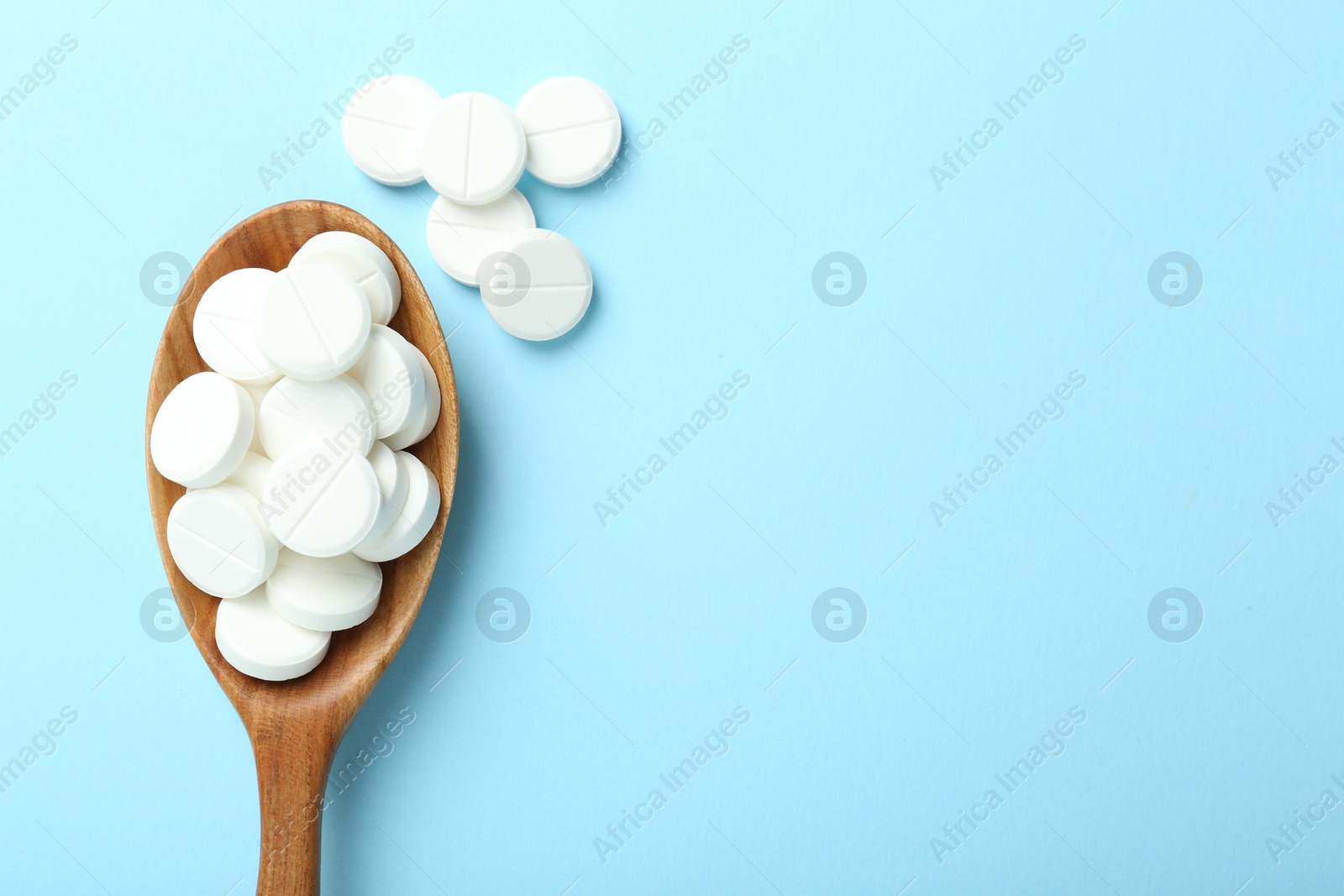 Photo of Antibiotic pills and spoon on light blue background, flat lay. Space for text