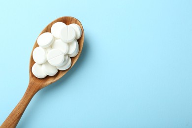 Photo of Antibiotic pills in spoon on light blue background, top view. Space for text