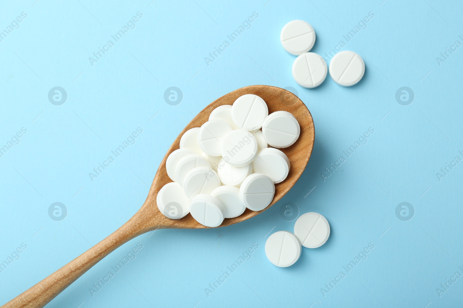 Photo of Antibiotic pills and spoon on light blue background, flat lay