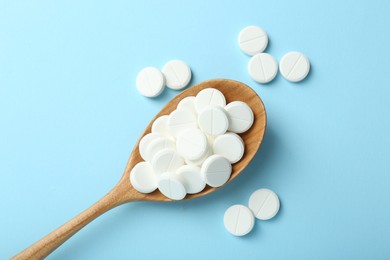 Photo of Antibiotic pills and spoon on light blue background, flat lay