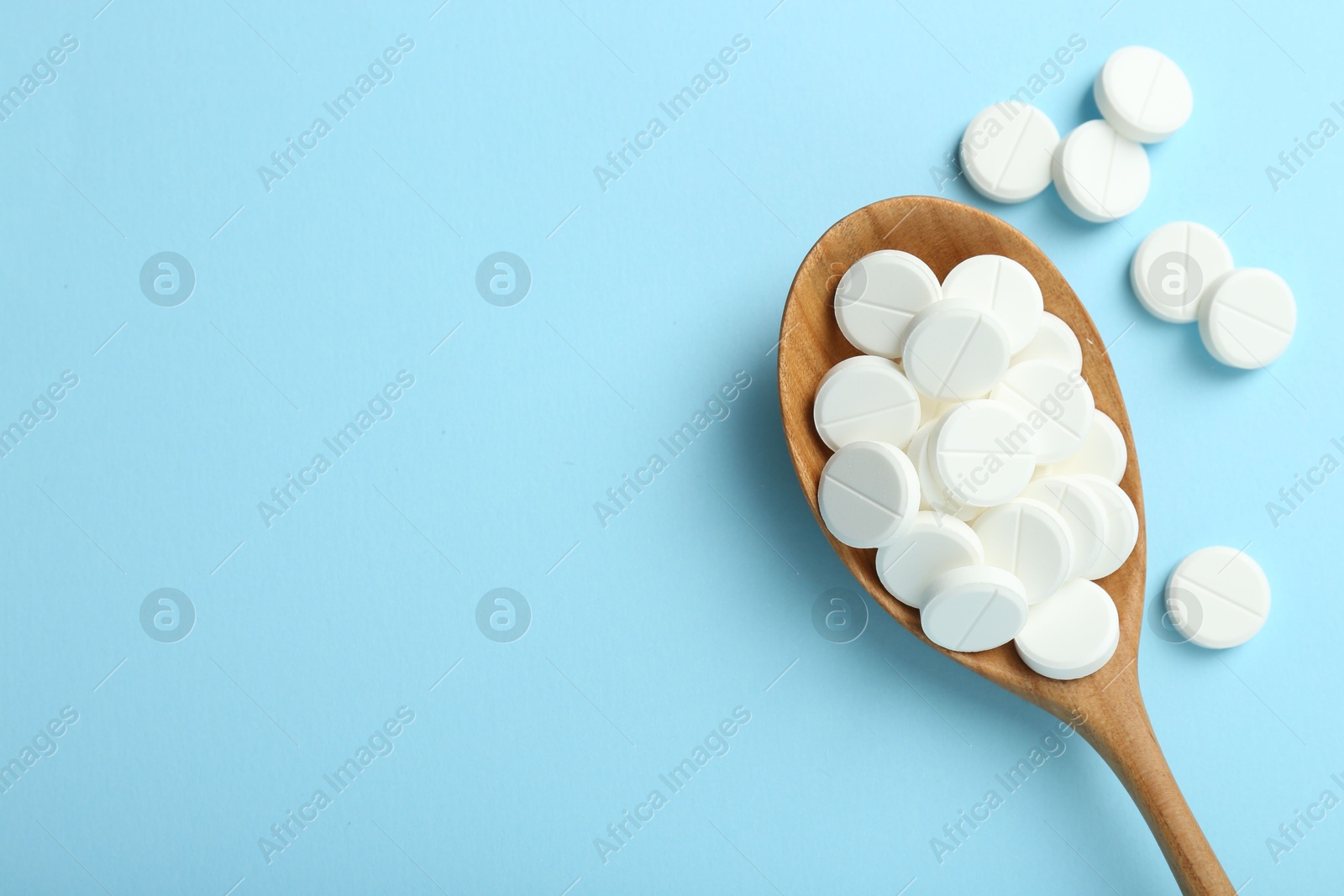 Photo of Antibiotic pills and spoon on light blue background, flat lay. Space for text