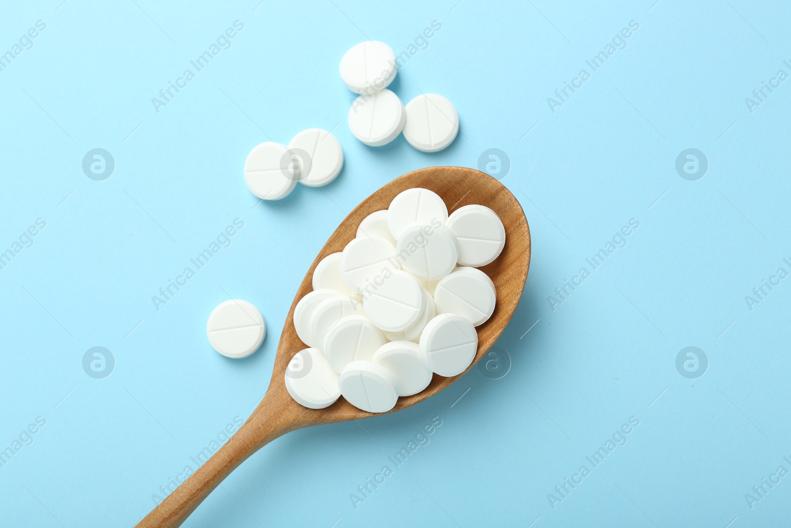 Photo of Antibiotic pills and spoon on light blue background, flat lay