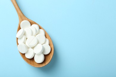 Antibiotic pills in spoon on light blue background, top view. Space for text