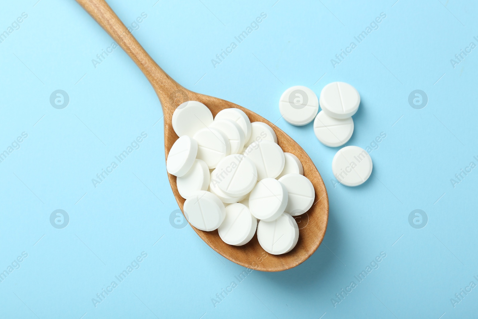 Photo of Antibiotic pills and spoon on light blue background, flat lay