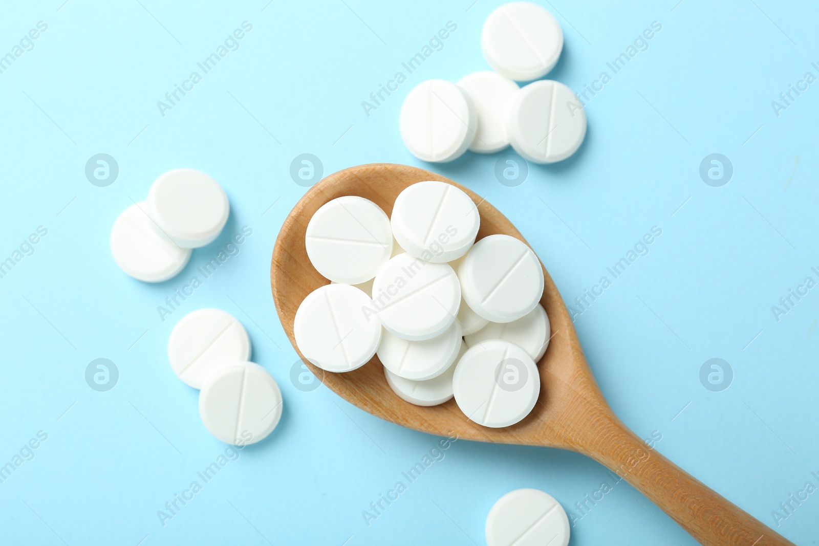 Photo of Antibiotic pills and spoon on light blue background, flat lay