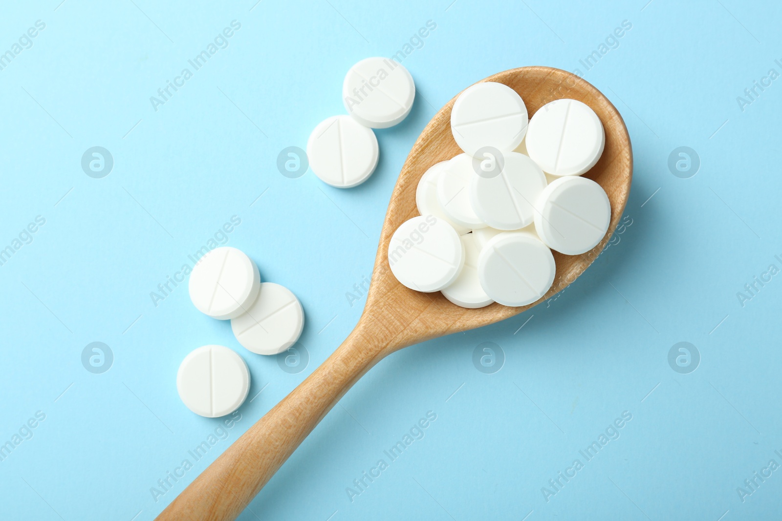 Photo of Antibiotic pills and spoon on light blue background, flat lay