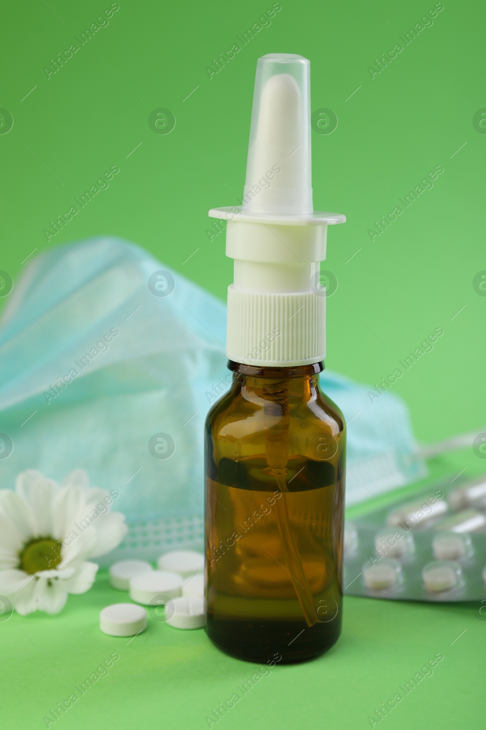 Photo of Allergy treatment. Nasal spray, pills, protective mask and flower on green background, closeup