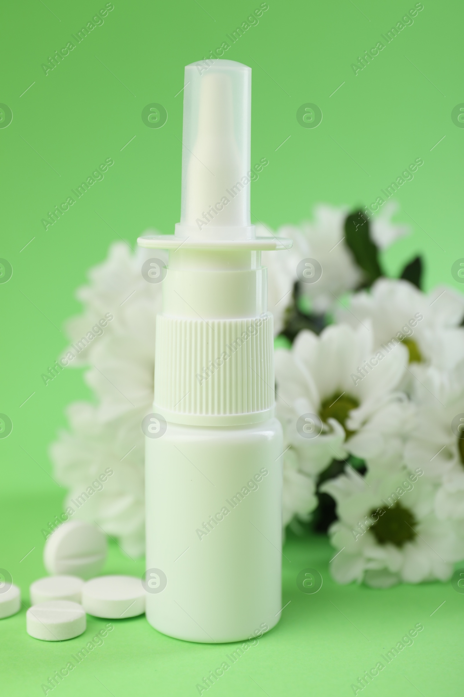 Photo of Allergy treatment. Nasal spray, pills and flowers on green background